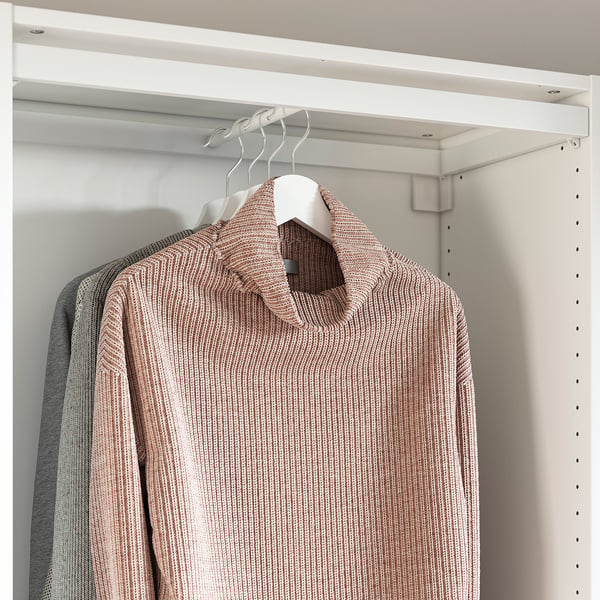 Beige sweater on hanger in white wardrobe with shelves and sliding doors.