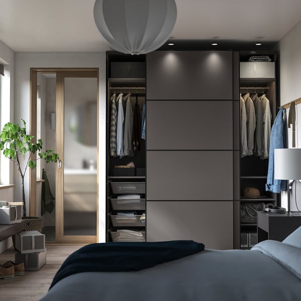 Modern bedroom with grey PAX wardrobe, sliding doors, mirror, and plant reflection.