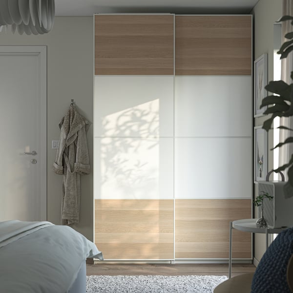 Modern bedroom with large PAX wardrobe in natural wood and white. Sliding doors save space, grey bed linens, hanging robe, and potted plant nearby.