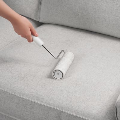 Person uses wide lint roller on light grey fabric surface.