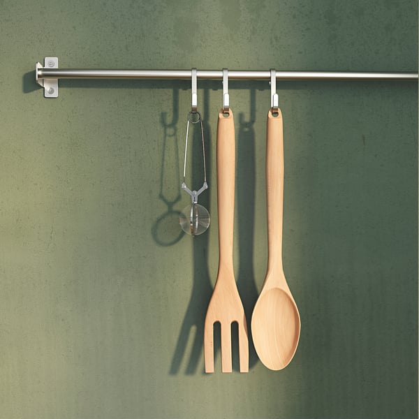 Three wooden utensils hang on hooks: spoon, fork, strainer. Green wall background.