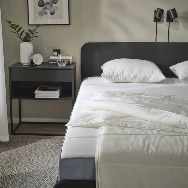 Bedroom with SANDGRÄSMAL duvet, bedside table with clock and books.