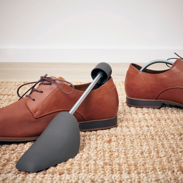 Brown leather shoes with connected black shoe shapers on beige woven rug.
