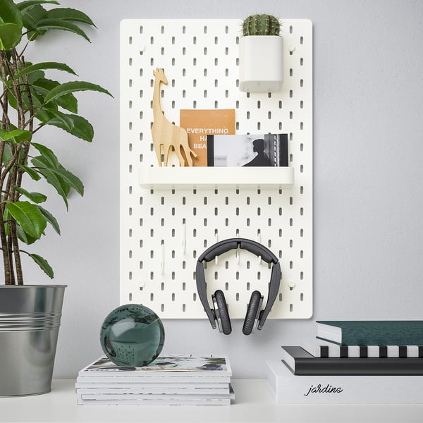 Wall-mounted SKÅDIS pegboard organises various items. Includes shelves, hooks, and planter, holding headphones, books, and decor.