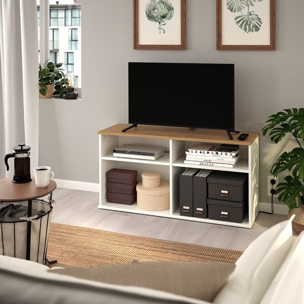 Wooden tv bench with white frame, tv, books, and coffee maker in a cosy living room.