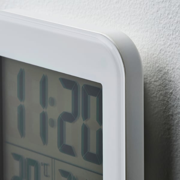 A close-up of a white digital alarm clock, displaying the time as 11:29. The clock is mounted on a wall with a sleek, minimalist design.