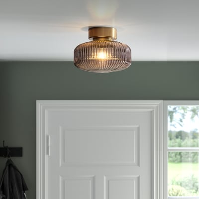 A modern, flush-mounted light fixture with a brass base and clear glass shade, providing warm, ambient light.