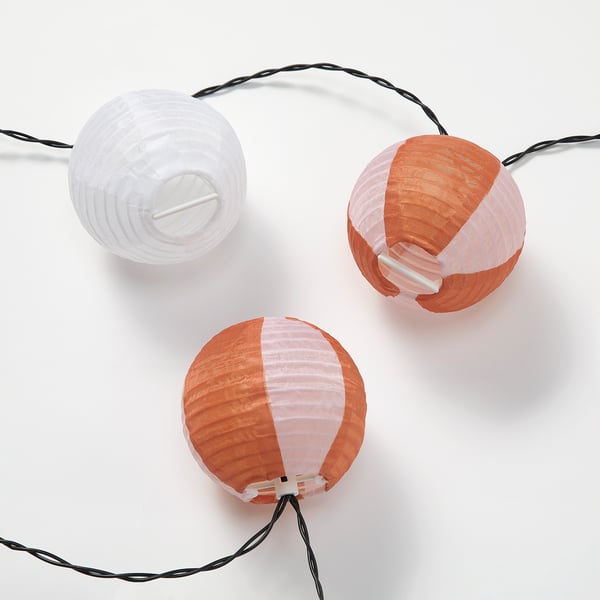 Three colourful solar-powered lanterns hang in a row, featuring orange and white dual shades, connected by black cords.
