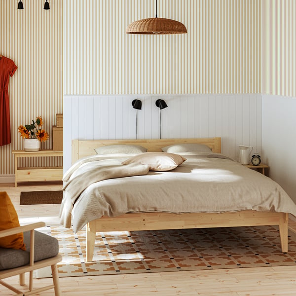 Modern bedroom: TAXÅSKLINT bed, beige linens, lights, decor, rug, plant, chair, striped wallpaper.