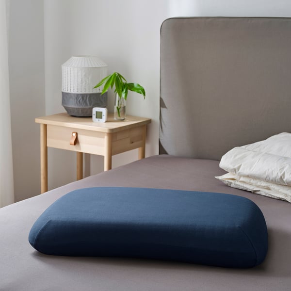 Bed with grey bedding, pillow, light, plant, and clock on bedside table.