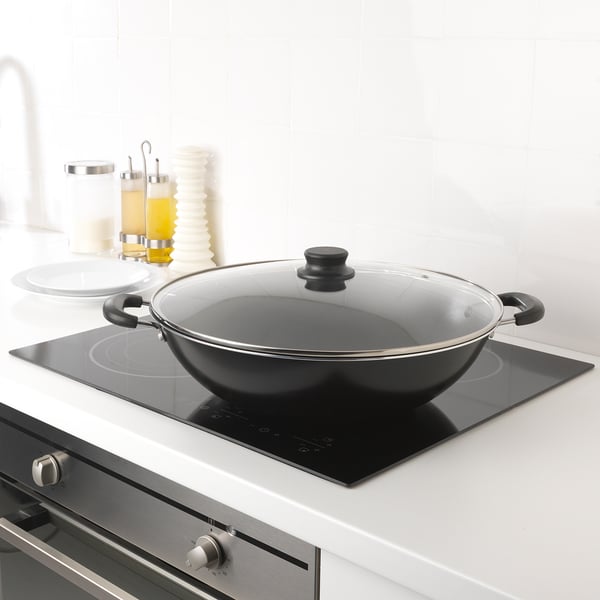 Modern kitchen with black wok on induction hob, two handles, white countertop, cooking tools.
