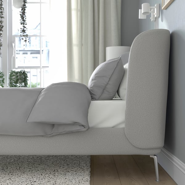 Modern bed with curved headboard, grey upholstery, adjustable sides, near window with lamp and plant.