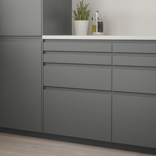 Modern kitchen with dark grey VOXTORP drawers, sleek handles, minimalist design. Small plant and oil bottles atop. Drawers larger than bottles.