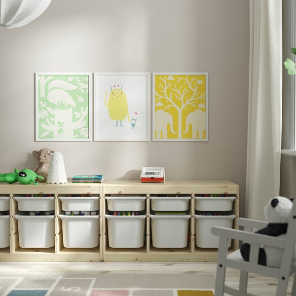 Tri barvite uokvirjene slike nad leseno polico s zabojniki, napolnjenimi z igračami.