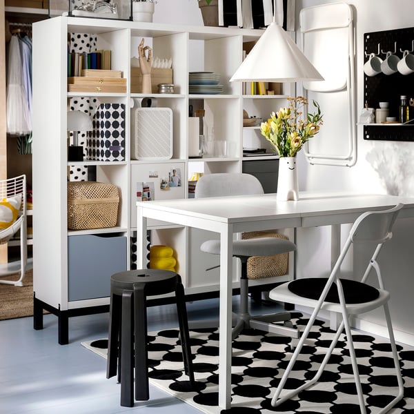 Sodobna jedilnica z belo mizo, stoli in črnim stolom. Svetlo osvetljena, z vzorčasto preprogo.