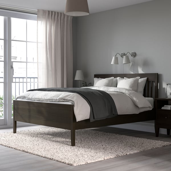 IDANÄS temno rjava lesena postelja z belo posteljnino v minimalistični sobi.
