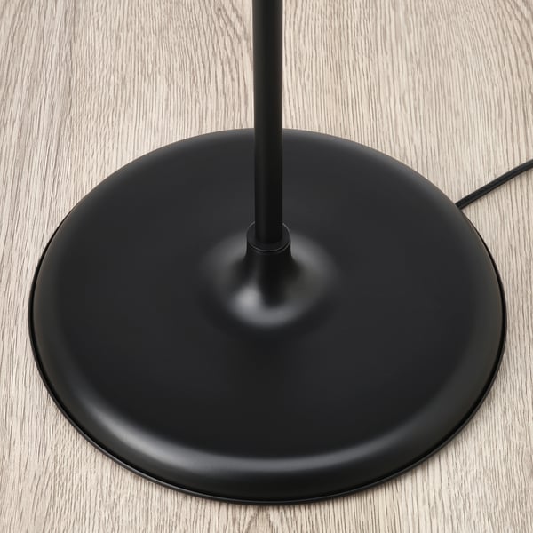 Sodobno podnožje talne svetilke iz črnih materialov, ki sedi na svetlih lesenih tleh.
