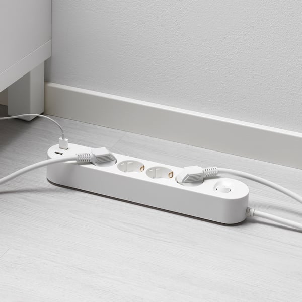 Bela večnamenska vtičnica z USB vrati na lesenih tleh. Priključena sta dva kabla, eden z belim priključkom.