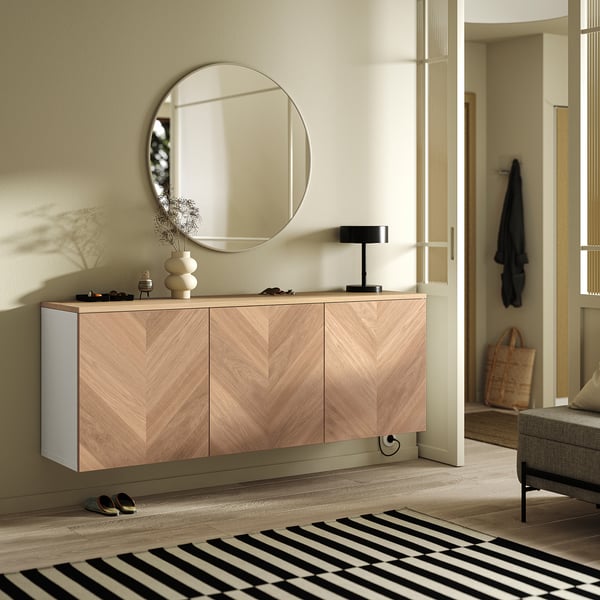 Ogledalo KVALMSÖ z aluminijastim okvirjem nad leseno omarico, odsevajoče cvetje, svetilka, sončna očala in črno-bela preproga.