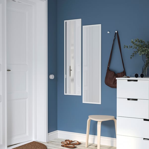 Sodobno modra soba z navpičnim ogledalom LILJETRÄD, belo komodo, torbico, rastlino, stolom in sandali.