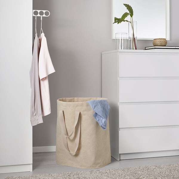 Bež torba za perilo z ročaji v bližini garderobe, ki drži modro oblačilo na preprogi.