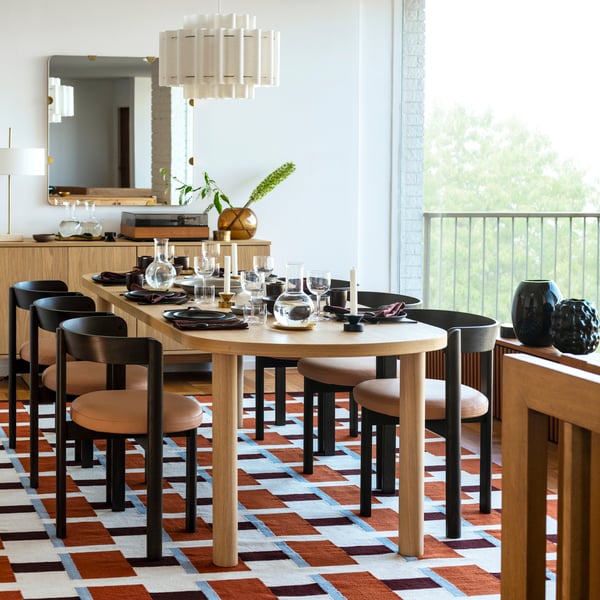 Sodobna jedilnica z leseno mizo, črnimi stoli, barvitimi preprogami, rastlinami in minimalističnim skandinavskim dekorjem.