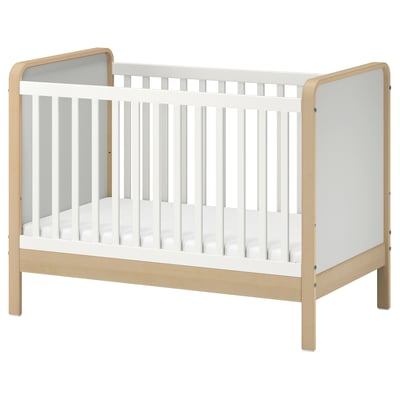 Wooden baby crib with white sides, minimalist design, rounded edges, vertical slats.