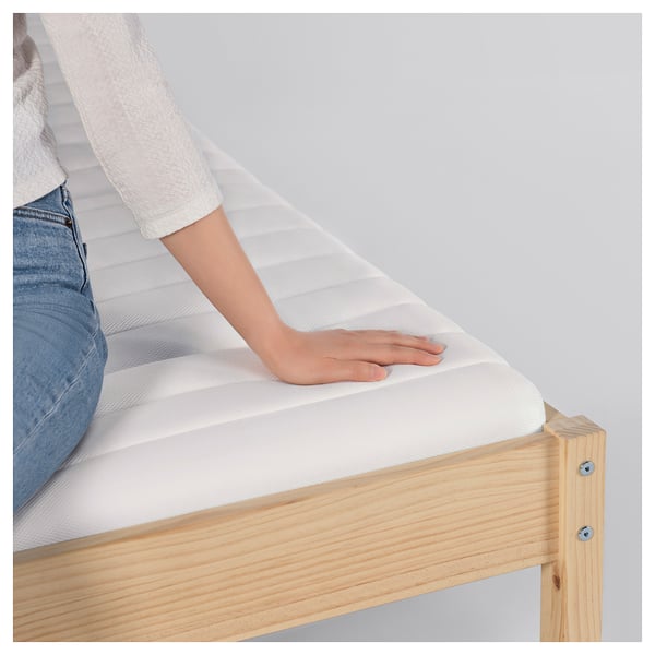 A person showing a white ÅNNFJÄLLET mattress on a wooden bed frame.