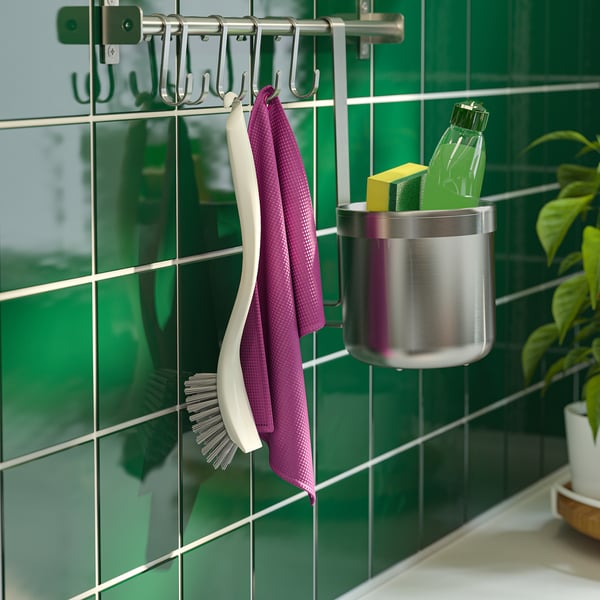 Metal rack with purple towel, white brush, and green bottle hanging on green tiled wall.
