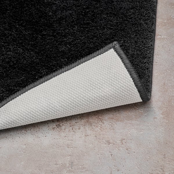Black bath mat corner, white latex backing visible, soft texture.