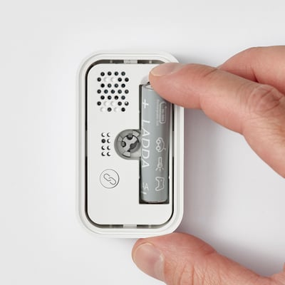 Hand placing battery into BADRING water leak sensor. Small, white device with speaker and sensors.