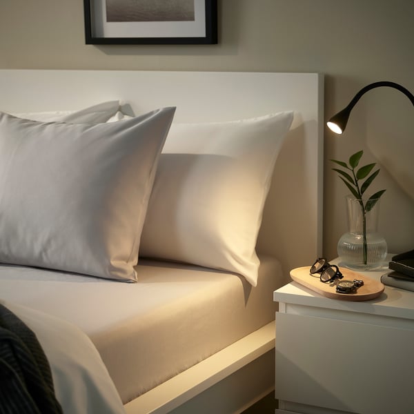 Bed with grey BÄRGLIM fitted sheet on a white bed frame. Sheet is soft, made from recycled polyester, and fits mattresses up to 16 cm thick.