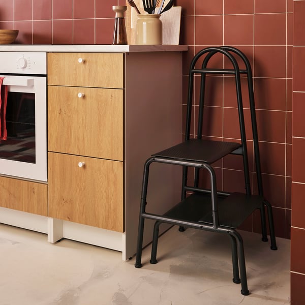 Kitchen with BÄSINGEN grey 2-step stool, wooden cabinet, oven, and terracotta tiles.