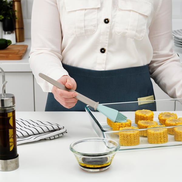A person uses a brush to coat honeycomb-shaped pastry with oil from a glass bowl, ready for baking, on a kitchen counter.