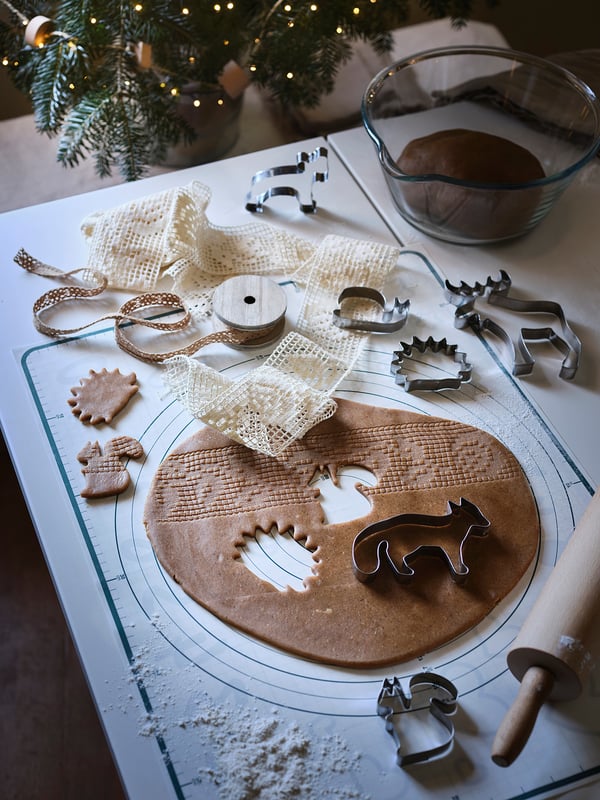 Baking setup with gingerbread dough on mat, cookie cutters, ribbon, and rolling pin. Festive, diy holiday scene.