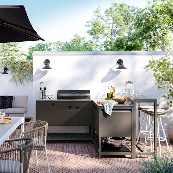 Outdoor kitchen with BÅTSKÄR table, grill, and seating. Modern, sturdy design ideal for dining and cooking.