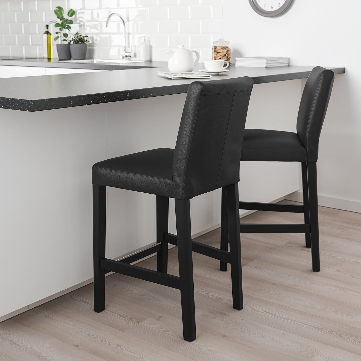Modern kitchen with sleek countertop, plant, tea set, & black bar stools.