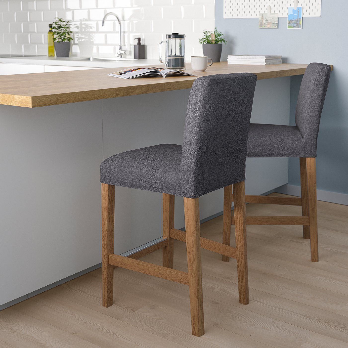 Grey barstool with wood legs, cushion, counter, coffee, dishes, plants.