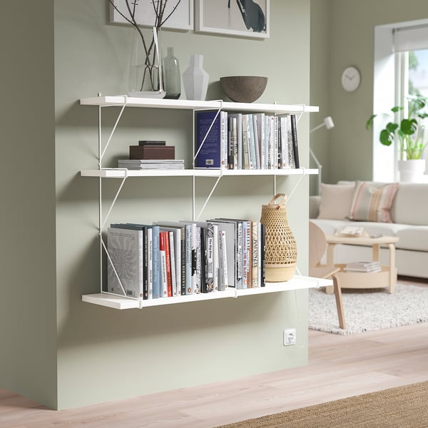White BERGSHULT shelf with books & decor against green wall.