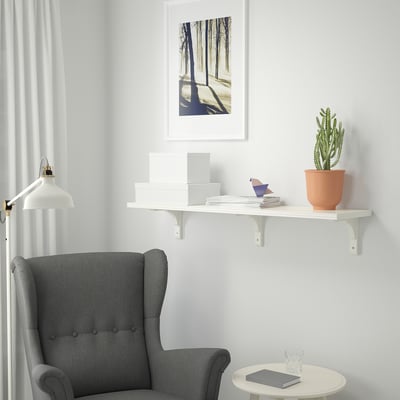 Reading corner with BERGSHULT shelf, books, plant, armchair, table, art, lamp.