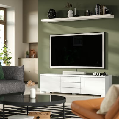 Modern living room: white BESTÅ BURS tv bench, flat-screen tv, green walls, bookshelves, patterned rug, round coffee table, grey armchair.