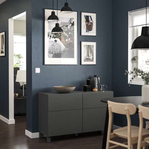 Modern living room with dark blue walls, grey BESTÅ unit, photos, & lights.