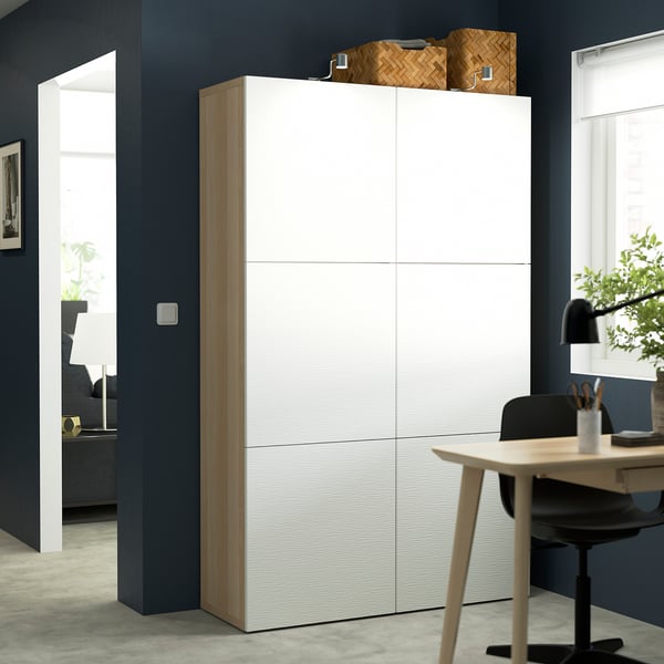 Modern BESTÅ cabinet with woven baskets, tall against dark wall.