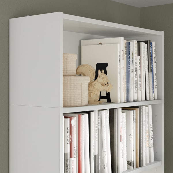 White BILLY bookshelf with adjustable shelves, holding several books and decorative items, including a wooden horse and woven baskets.