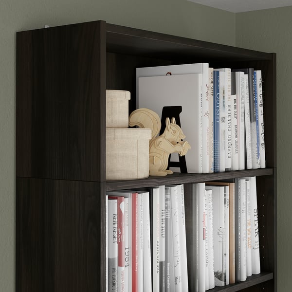 Dark wooden bookshelf against green wall, filled with books and decorative items.