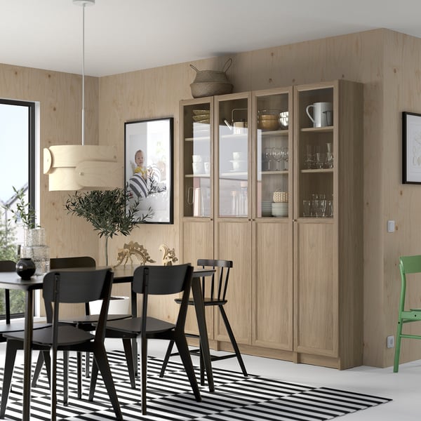 Natural wood BILLY bookcase with glass, dining set, and rug. Decor includes picture and wall light.