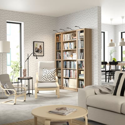 Modern living room with BILLY bookcase; light wood, large, filled with books. Accompanied by chairs & couch.