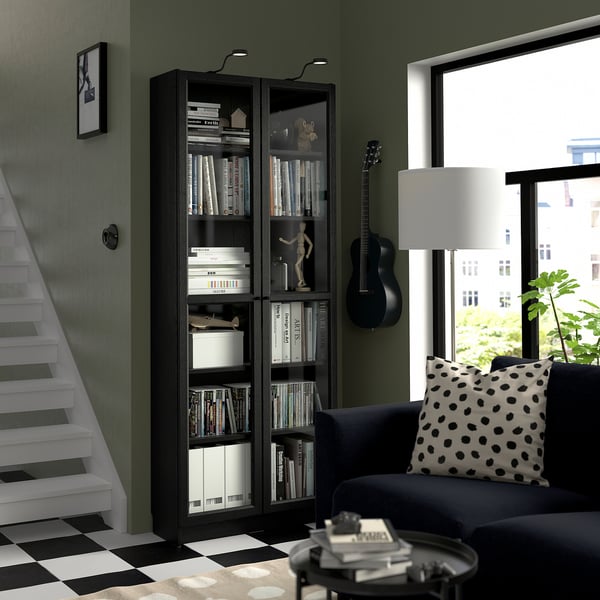 Dark wood BILLY bookcase with guitar, sofa & staircase in monochrome room.