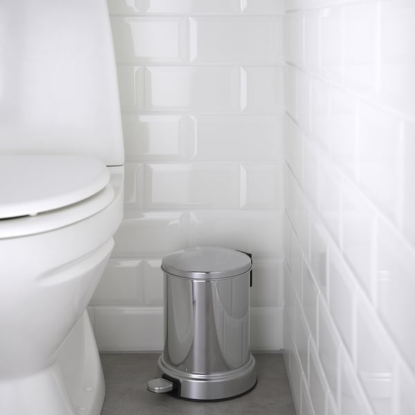 Silver pedal bin beside a white toilet, with a slow-closing lid. The bin has a round shape and chrome details, suitable for bathrooms.