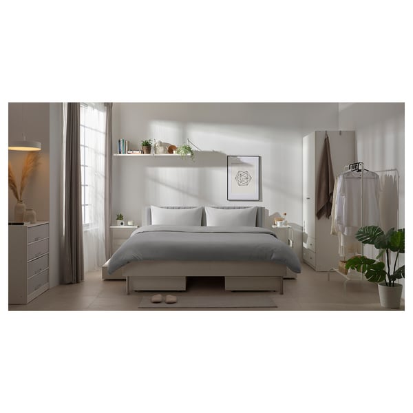 Minimalist white bedroom with grey bedding, plants, and modern decor.